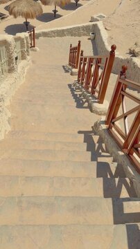Ancient stone staircase with wooden railing leading to sandy beach in warm sunlight Egypt. Hurghada
