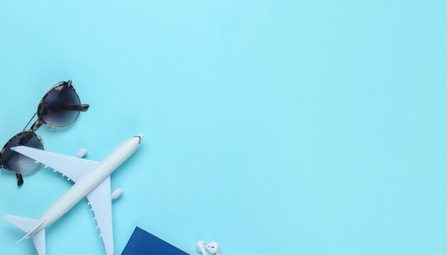 Travel concept flat lay featuring a toy airplane, passport and sunglasses on a blue background