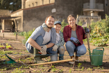 Obraz premium Family of farmers with a watering can and a hoe in the garden after planting seeds. Farmers grow organic and organic vegetables. Portrait of a family on a farm