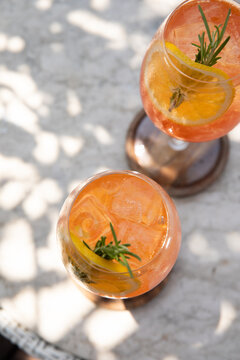 two glasses of aperol spritz garnished with rosemary and orange on a sunny day on restaurant patio