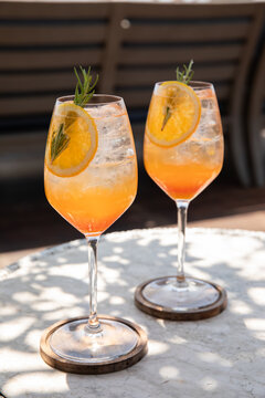 two glasses of aperol spritz garnished with rosemary and orange on a sunny day on restaurant patio