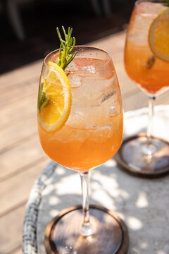 two glasses of aperol spritz garnished with rosemary and orange on a sunny day on restaurant patio