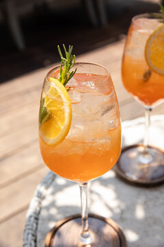 two glasses of aperol spritz garnished with rosemary and orange on a sunny day on restaurant patio