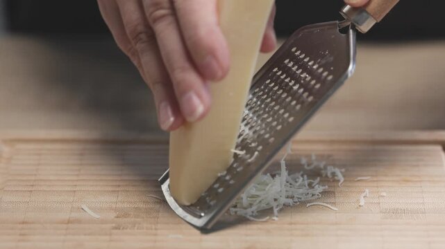 Chef grates hard cheese onto a wooden cutting board while preparing ingredients for a homemade meal in the kitchen