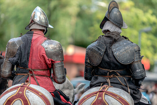 Rear view of two&nbsp; soldiers in steel armor and morion helmets riding horses during a historical reenactment festival.