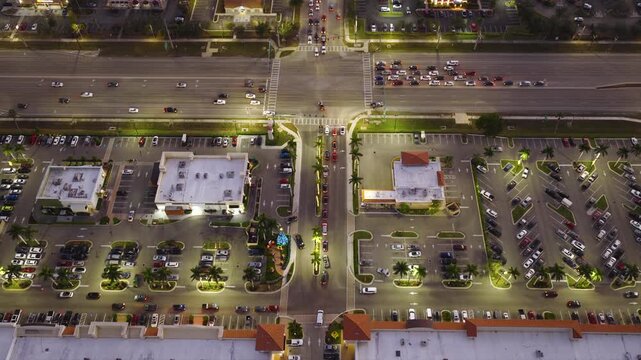 Aerial view of crowded shopping mall parking lot in Florida at night, filled with vehicles and busy traffic. Consumer activity, retail demand and urban commercial lifestyle.