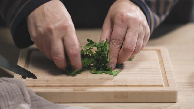 chef is chopping parsley leaves on a wooden kitchen board to prepare a healthy meal,  food closeup. Ingredients for tomato pasta
