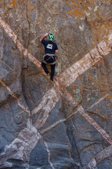 Athletic rock climbers scaling a high vertical crag marked by striking geometric white mineral dykes in an arid canyon landscape. © Valentin