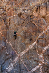 Athletic rock climbers scaling a high vertical crag marked by striking geometric white mineral dykes in an arid canyon landscape. © Valentin