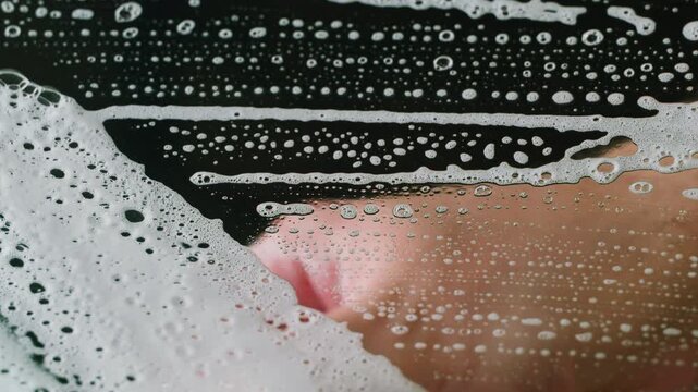 Cleaning foam streaks on black glass, washing dirty window surface with soap suds, glass cleaning service and housework close up macro