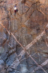 Athletic rock climbers scaling a high vertical crag marked by striking geometric white mineral dykes in an arid canyon landscape. © Valentin