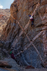 Athletic rock climbers scaling a high vertical crag marked by striking geometric white mineral dykes in an arid canyon landscape. © Valentin