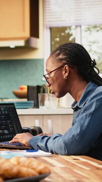 Vertical video: Woman works on programming and software development tasks. Laptop screen displays code, scripts and binary data, illustrating remote system maintenance in a high-tech occupation.