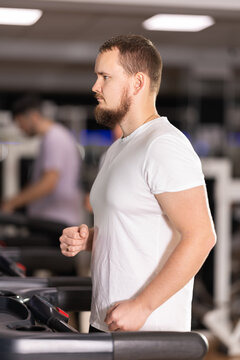 Bearded man hardly perform exercise on treadmill and running during fitness class. Fitness equipment, visitors engaged in physical task during training and perform brisk walking on treadmill