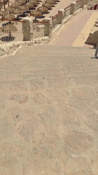 Stone steps leading to sunlit beach with straw umbrellas and lounge chairs Egypt. Hurghada
