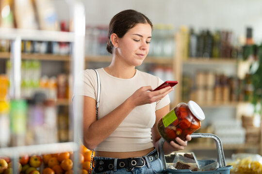 Woman customer at shop scan QR code on pickled tomatoes package using phone camera. Client study composition, manufacturer information of product using application.