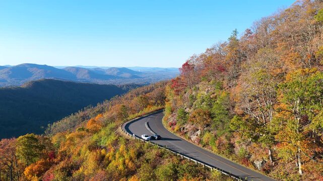 Blue Ridge Parkway scenic overlook in North Carolina with parked vehicle surrounded by brilliant red, orange and golden autumn colors.