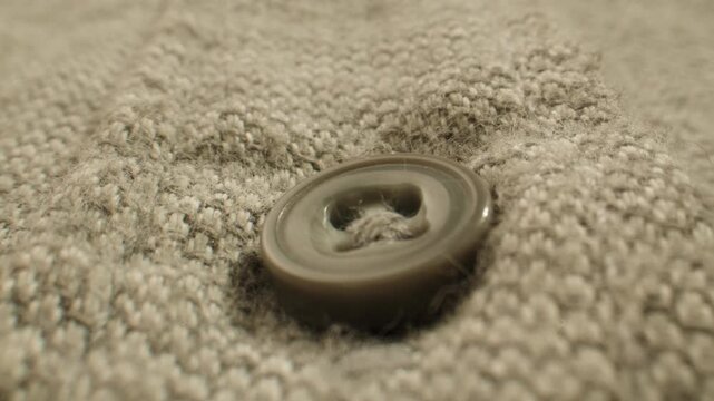 Sweater button on beige wool knit, knitted cardigan texture extreme close up macro, knitwear detail for clothing factory and garment production