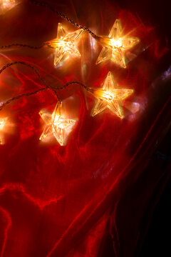 Cozy Christmas Decoration.Glowing Star Shaped Fairy Lights on Red Fabric. decorative LED lights