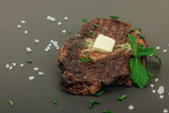 Grilled ribeye steak with melted butter and herbs on dark background, high protein meal concept