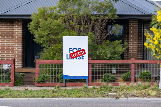 A "For Lease" real estate signboard with a red "LEASED" sticker displayed in front of a suburban house and garden in Australia. Concept of rental demand, housing shortage and real estate