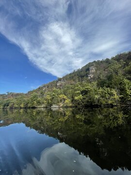 Calm lake reflecting forested bluff under wispy clouds
