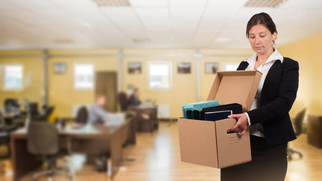 Employment termination, office worker carries a box of personal belongings after losing her job, layoffs, dismissal, redundancy and unemployment.