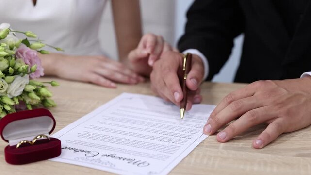 Couple signing marriage contract at wooden table indoors, closeup