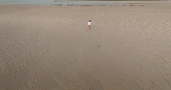Woman walking barefoot on a wide sandy beach during low tide in Ko Lanta, Thailand, expressing concepts of solitude, travel, freedom, and escape on tropical coastline. Aerial view drone shot panorama
