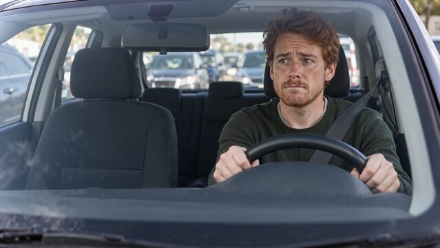 Anxious young man driving car in congested traffic. Worried red-haired male commuter behind steering wheel. Mental health and driving phobia concept