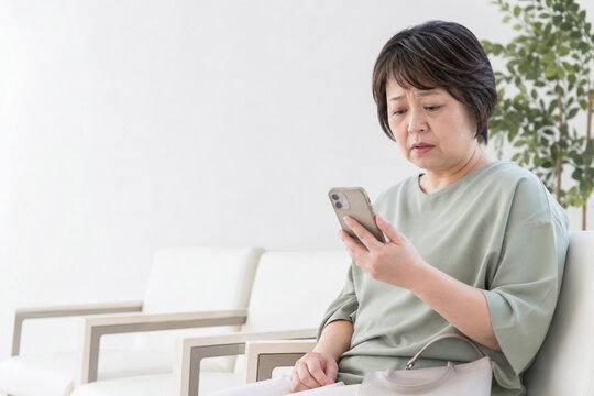 待合室でスマートフォンを見て不安になる中年女性