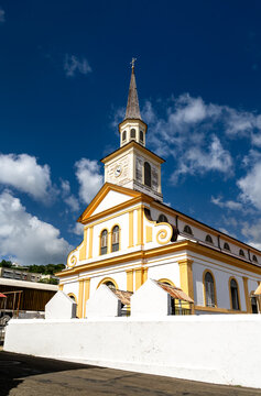 The historic yellow and white facade of Saint Jacques Church under a blue sky in Le Carbet, Martinique.