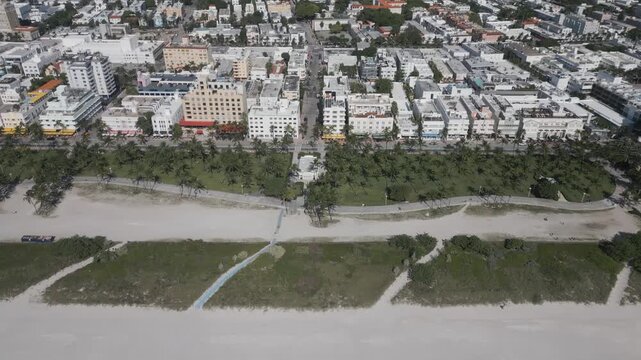 Aerial glide past miami beach rooftops bordering a sandy dune strip