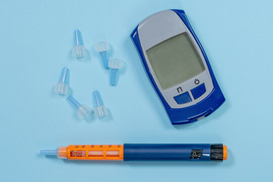 An orange insulin pen, a portable blood sugar meter and scattered sterile needle caps lie on a soft blue surface, a concept of everyday self management and patient education.
