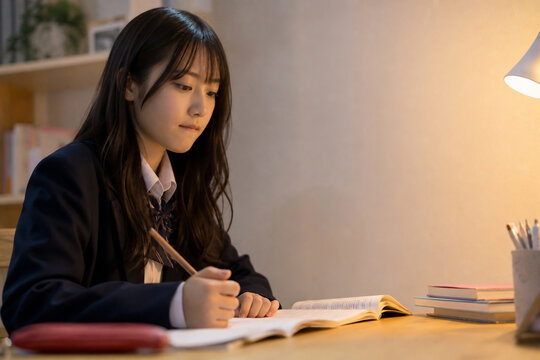 夜の自室で制服を着てデスクで教科書に向かい勉強する日本人女子高生