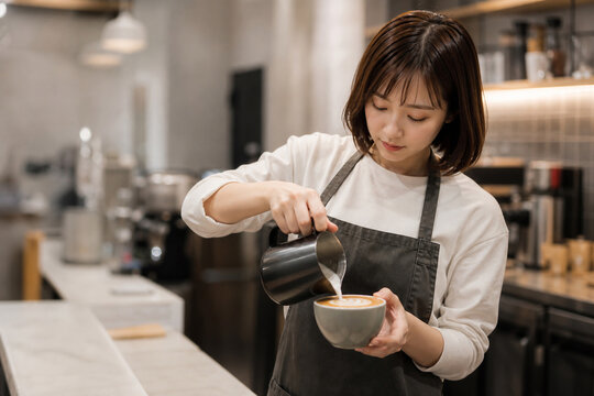 カフェのカウンターでラテアートを注ぐ日本人バリスタ女性