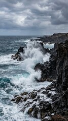 Fototapeta premium Powerful ocean waves crashing against rugged dark volcanic rocks on a stormy coast.