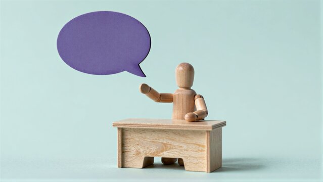 Wooden figure sits at desk, speaking with purple speech bubble above its head.