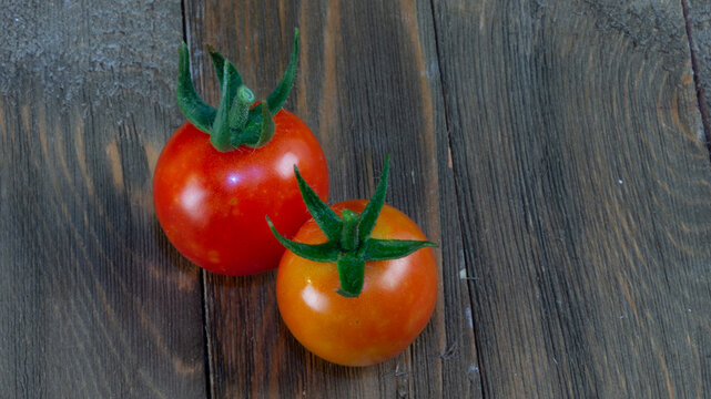 Two freshly picked tomatoes at different stages of ripeness on rustic wood.