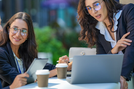 A team of three Hispanic businesswomen in matching dark suits, deep in an animated discussion, run through a presentation at an evening meeting, a modern corporate lifestyle scene.