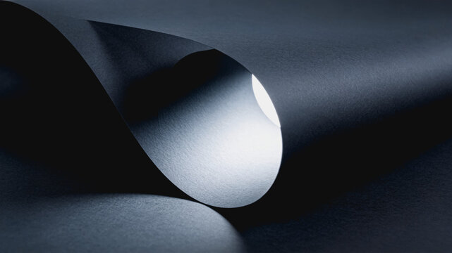 A dark gray thin sheet curved and rolled into a cylinder, showing smooth texture and soft shadows in a minimalist close-up.