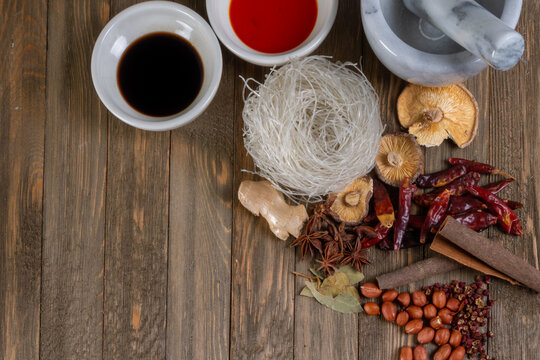 Overhead arrangement of noodles, sauces, dried chilies, spices, mushrooms, ginger and peanuts on rustic wood.
