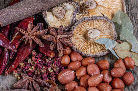 Dried chilies, mushrooms, star anise and peanuts arranged on a rustic wooden surface.