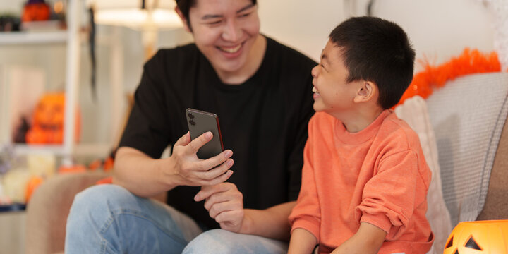 Asian father and son using smartphone together during Halloween at home