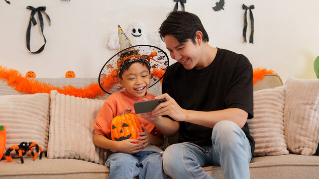 Asian father and son looking at smartphone together during Halloween celebration