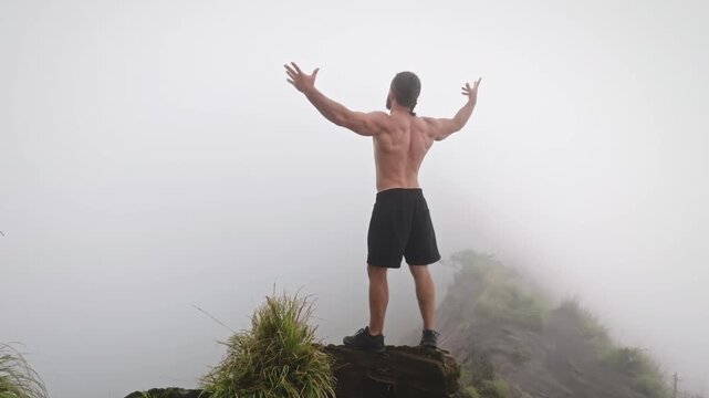 Muscular man standing shirtless on a misty mountain peak, arms raised in triumph, feeling freedom and achievement after a challenging ascent on mount Batur, Bali. Outdoor active sports and recreation