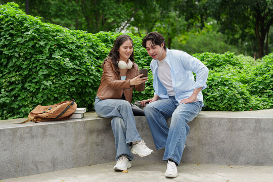 Asian university students looking at mobile phone screen together outdoors