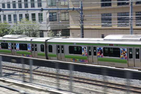 Green Yamanote line commuter train with Disney character advertisement moving fast.