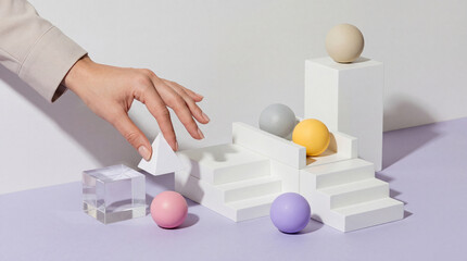 Obraz premium Female Hand Placing White Pyramid on Minimalist Geometric Stairs with Colorful Spheres and Glass Cube, Concept of Business Growth, Structural Strategy, Creative Building and Organization