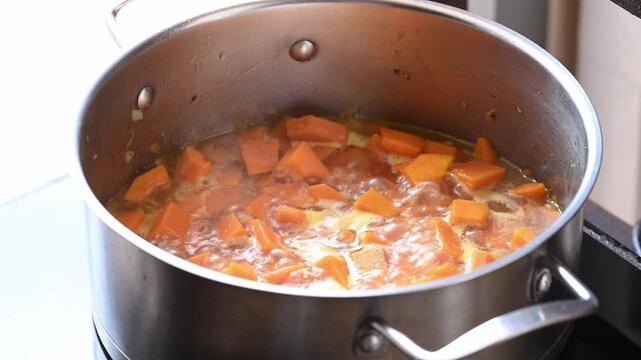 Boiling butternut squash in vegetable broth inside a pot to make butternut squash soup, homemade food in autumn